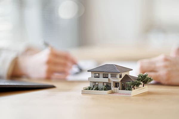 書類に記入する手元と家の模型 不動産業イメージ写真